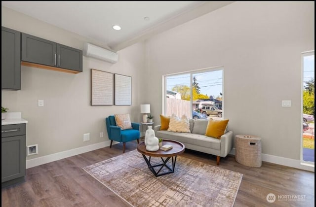 living room with a wealth of natural light, wood finished floors, a wall mounted AC, and baseboards