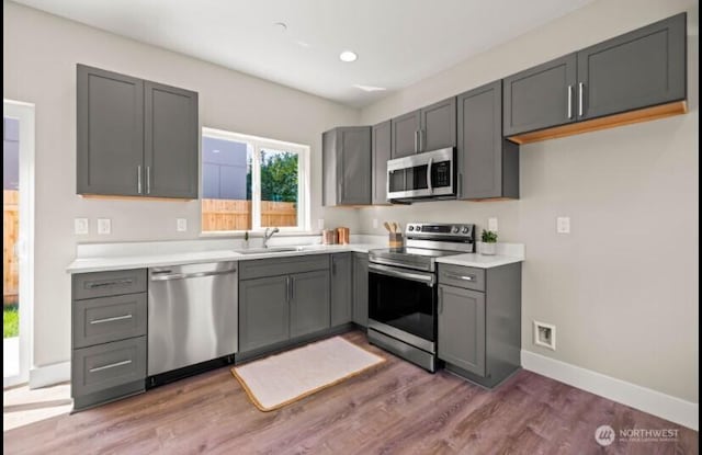 kitchen featuring stainless steel appliances, light countertops, a sink, light wood-style floors, and baseboards