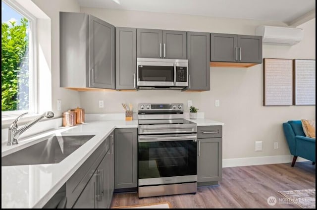 kitchen featuring a wall mounted AC, gray cabinets, stainless steel appliances, and a sink