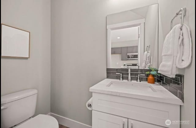 half bathroom featuring toilet, vanity, and baseboards