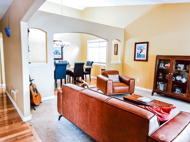 living area featuring arched walkways, vaulted ceiling, wood finished floors, baseboards, and an inviting chandelier