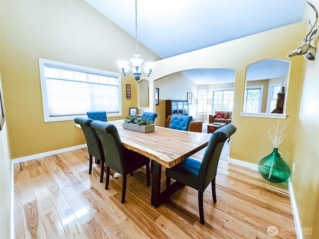 dining room featuring arched walkways, baseboards, high vaulted ceiling, light wood finished floors, and a chandelier