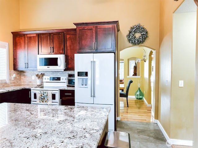 kitchen with arched walkways, tasteful backsplash, light stone counters, baseboards, and white appliances