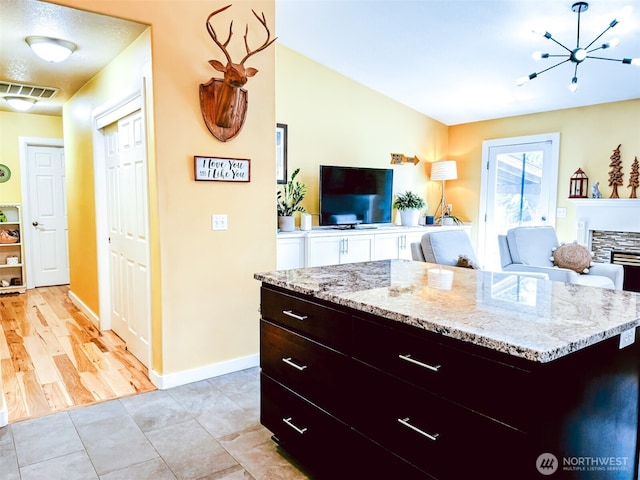 kitchen featuring baseboards, light stone countertops, a chandelier, and open floor plan