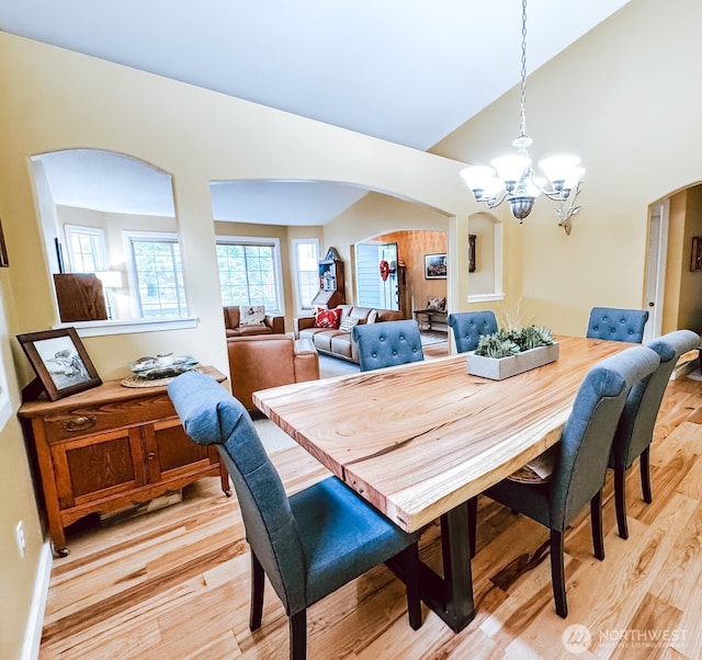 dining area with an inviting chandelier, arched walkways, light wood-style floors, and lofted ceiling