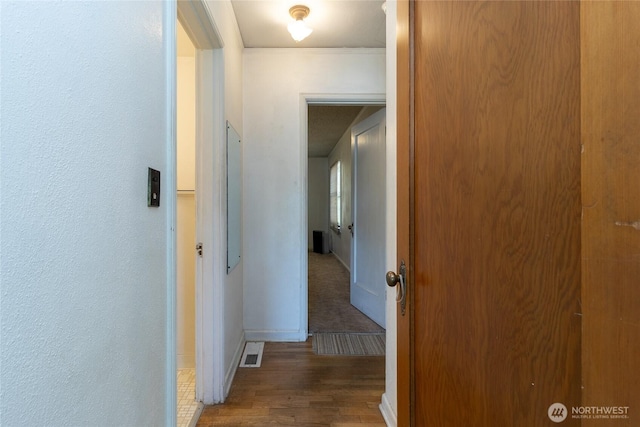 corridor featuring baseboards, visible vents, and wood finished floors