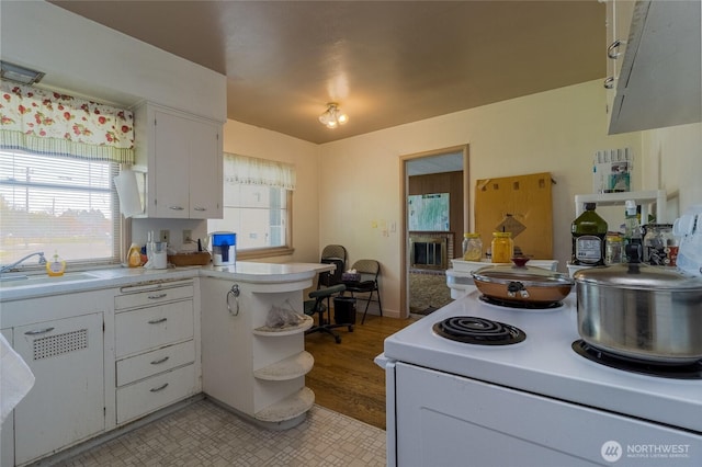 kitchen with a sink, white electric stove, white cabinetry, and a wealth of natural light