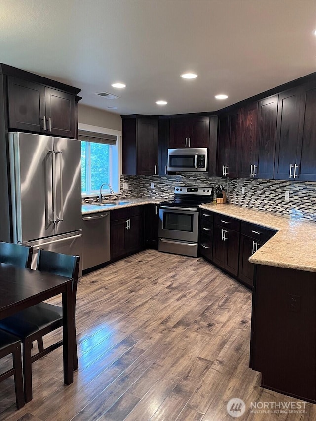 kitchen featuring stainless steel appliances, decorative backsplash, a sink, and wood finished floors