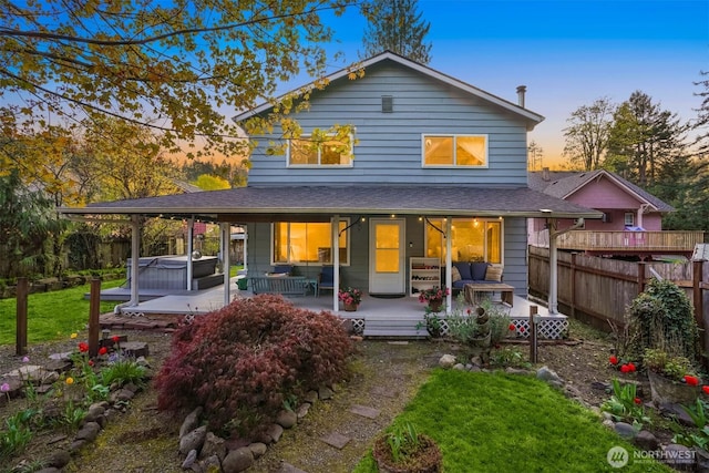 rear view of property featuring roof with shingles, covered porch, fence, a lawn, and a hot tub