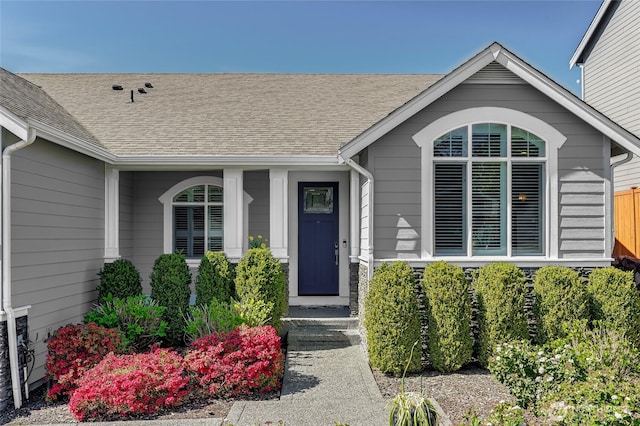 view of exterior entry with fence and a shingled roof