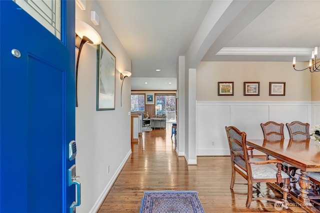 entryway with an inviting chandelier, crown molding, wood finished floors, and a wainscoted wall