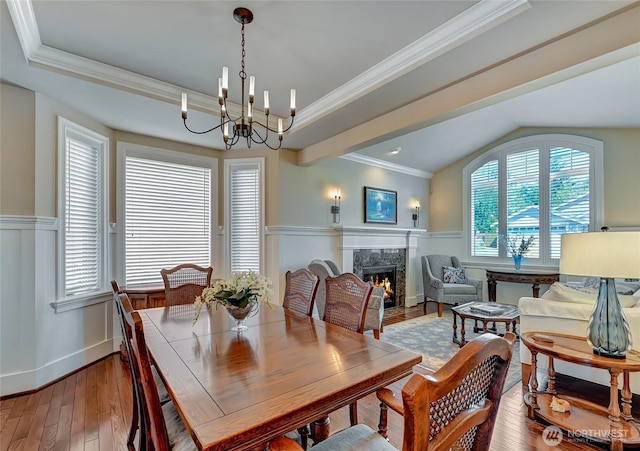 dining space with wainscoting, wood-type flooring, a chandelier, a high end fireplace, and vaulted ceiling