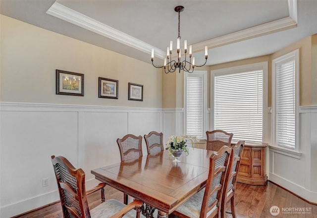 dining area featuring an inviting chandelier, a raised ceiling, ornamental molding, and wainscoting