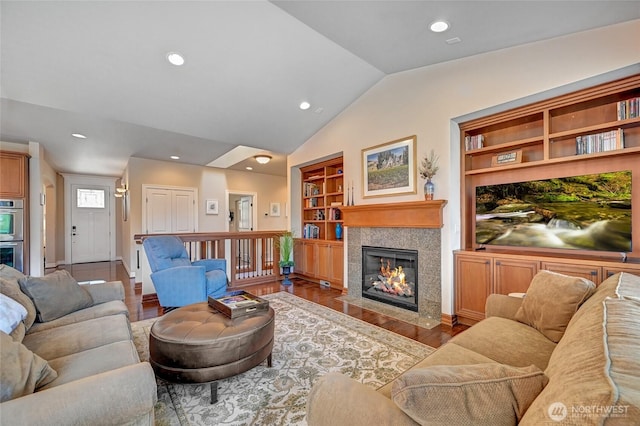 living area featuring built in shelves, baseboards, wood finished floors, a tile fireplace, and vaulted ceiling