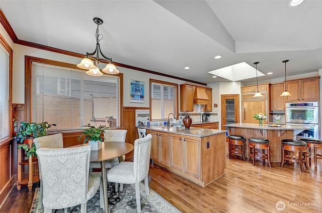kitchen with stainless steel double oven, a sink, a center island, paneled refrigerator, and custom exhaust hood