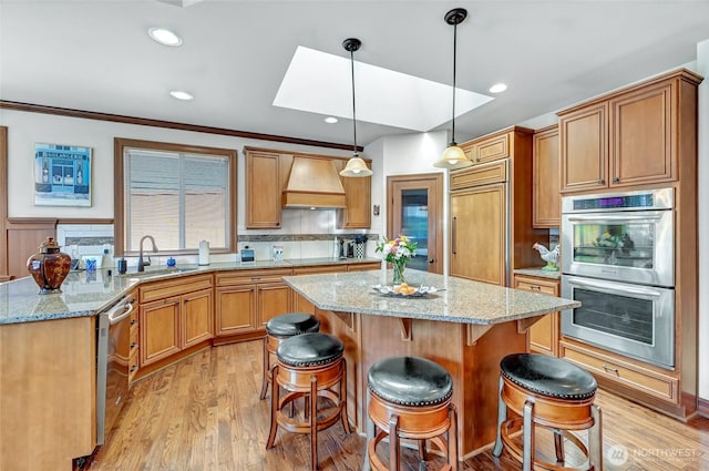 kitchen featuring a kitchen island, a skylight, a sink, custom exhaust hood, and stainless steel appliances