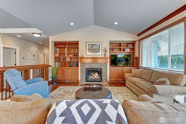 living area featuring built in shelves, recessed lighting, wood finished floors, lofted ceiling, and a tile fireplace