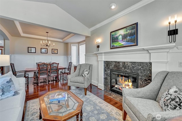 living room with a fireplace, wood finished floors, a wainscoted wall, an inviting chandelier, and ornamental molding