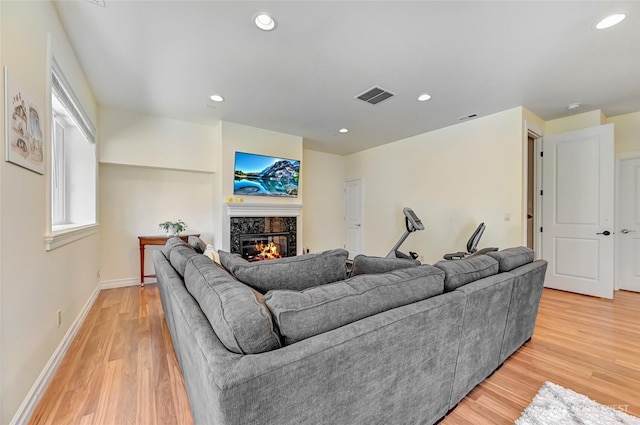 living room with visible vents, baseboards, a glass covered fireplace, light wood-style floors, and recessed lighting