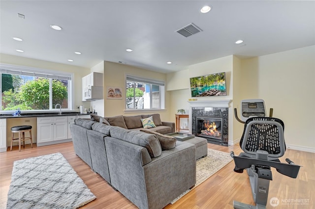 living room with a high end fireplace, plenty of natural light, light wood finished floors, and visible vents