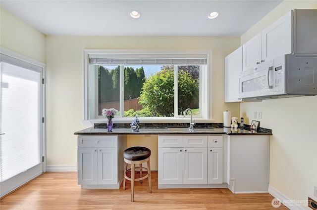 kitchen with white microwave, recessed lighting, white cabinetry, a sink, and light wood-style flooring