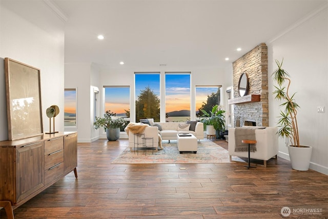 living area featuring a stone fireplace, recessed lighting, ornamental molding, and dark wood-style flooring