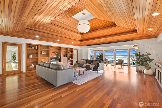 living area featuring a tray ceiling, wood finished floors, a water view, wooden ceiling, and crown molding