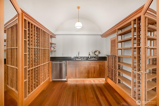 wine room with lofted ceiling, indoor wet bar, wood finished floors, and a sink