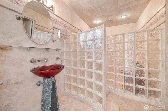 full bath with tile walls, tile patterned floors, walk in shower, and a sink