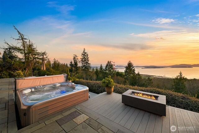 wooden terrace with a water view, an outdoor fire pit, and an outdoor hot tub
