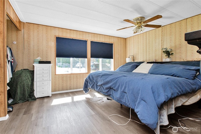 bedroom featuring baseboards, a ceiling fan, wood finished floors, and wallpapered walls