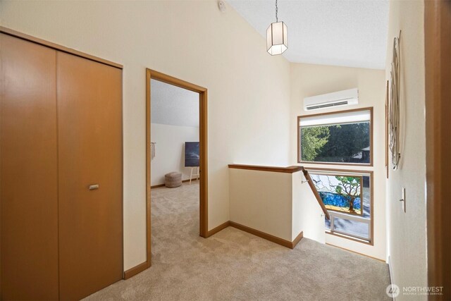 corridor featuring an AC wall unit, an upstairs landing, light carpet, high vaulted ceiling, and baseboards