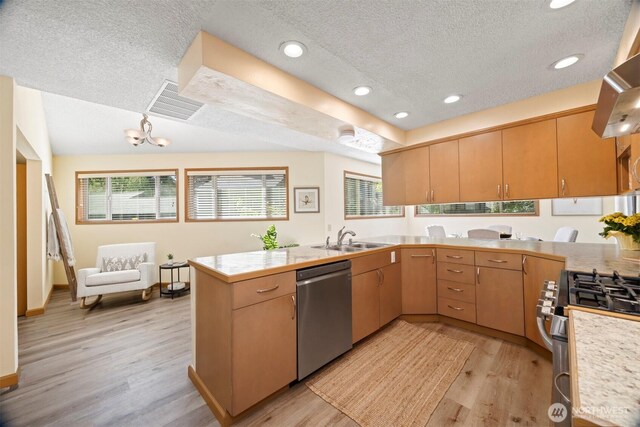 kitchen featuring stainless steel appliances, a textured ceiling, a sink, a peninsula, and light wood-type flooring