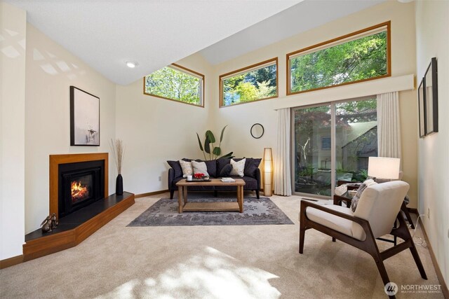 living room featuring carpet flooring, a high ceiling, a glass covered fireplace, and baseboards