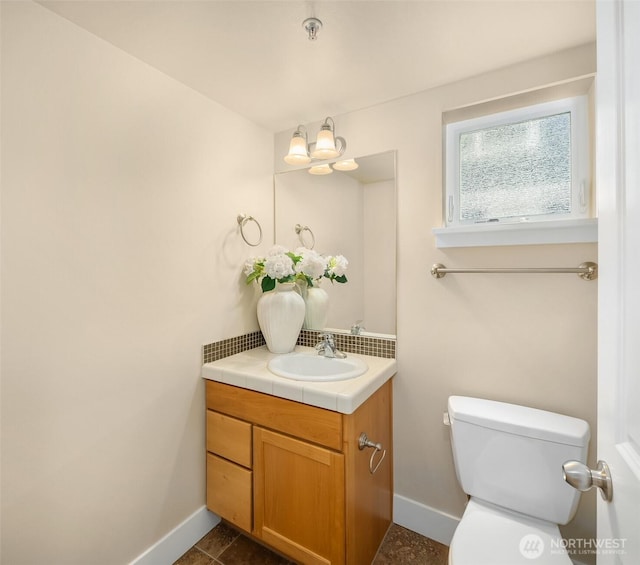half bath with toilet, baseboards, a notable chandelier, and vanity