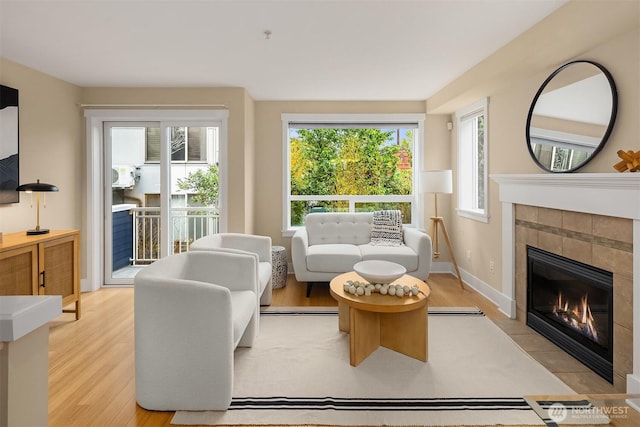 living room featuring baseboards, light wood-style flooring, and a tile fireplace
