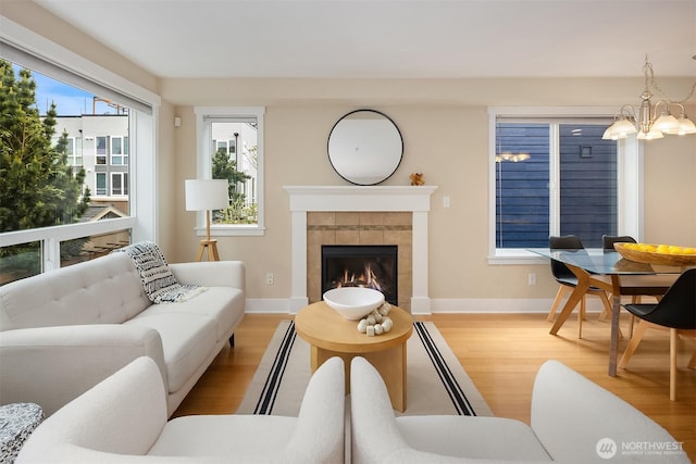 living area with light wood-style floors, baseboards, a fireplace, and an inviting chandelier