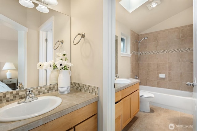 bathroom featuring vanity, toilet, lofted ceiling with skylight, tile patterned floors, and shower / washtub combination