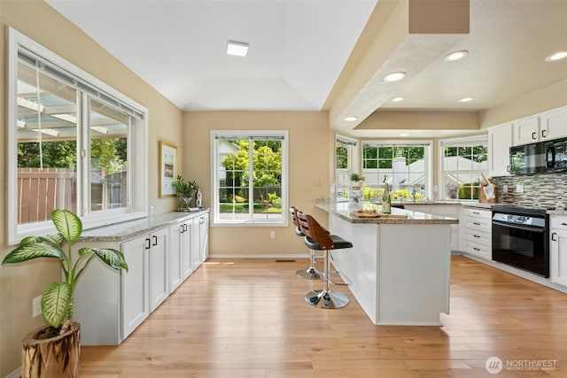 10116 SE 188th St, Renton, WA 98055 - kitchen featuring black microwave, light wood-style flooring, a breakfast bar area, white cabinets, and recessed lighting