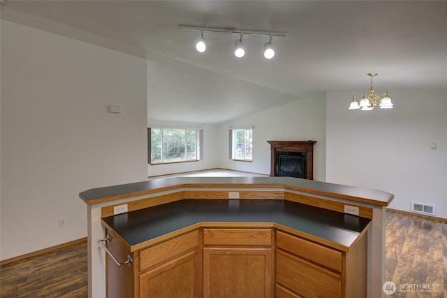 kitchen with dark wood-style floors, dark countertops, open floor plan, a glass covered fireplace, and visible vents