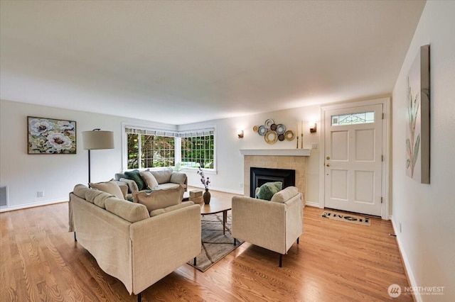 living room featuring light wood finished floors, a tiled fireplace, and baseboards