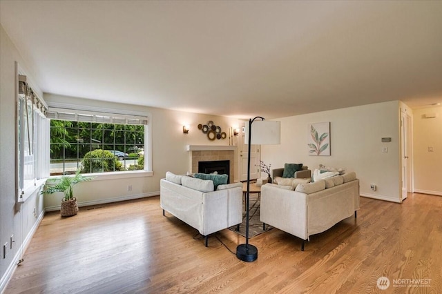 living room with light wood-style flooring, a tile fireplace, and baseboards