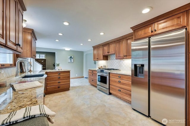 kitchen with appliances with stainless steel finishes, a sink, backsplash, light stone countertops, and recessed lighting