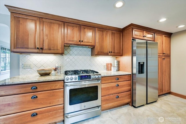 kitchen with appliances with stainless steel finishes, brown cabinets, backsplash, light stone counters, and recessed lighting