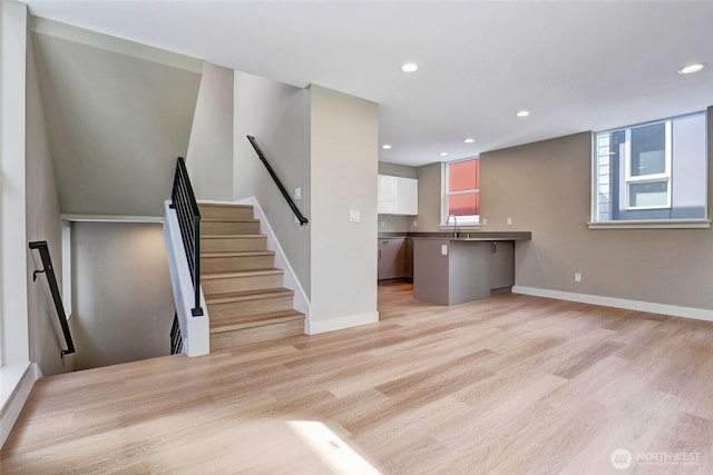 unfurnished living room with recessed lighting, light wood-style flooring, baseboards, and a sink