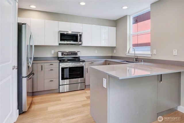 kitchen featuring recessed lighting, stainless steel appliances, a sink, light wood-type flooring, and a peninsula