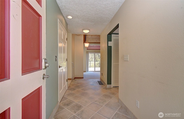 hallway featuring a textured ceiling, baseboards, and visible vents