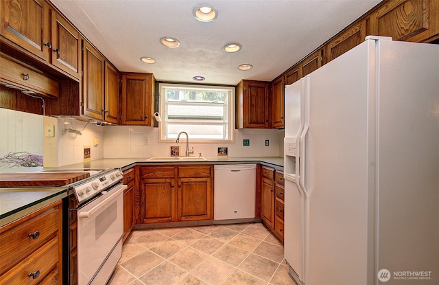 kitchen featuring recessed lighting, backsplash, a sink, white appliances, and brown cabinetry
