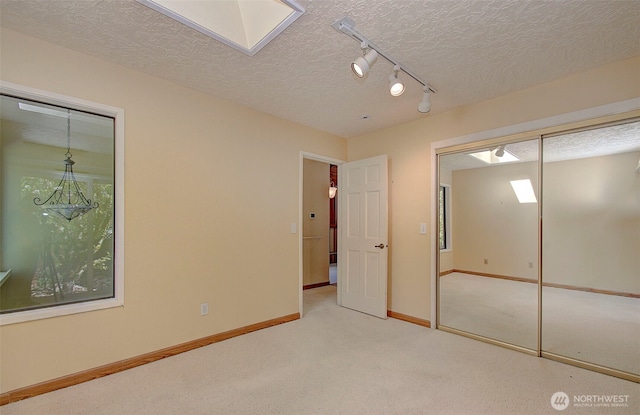 unfurnished bedroom featuring a textured ceiling, a skylight, carpet floors, rail lighting, and baseboards