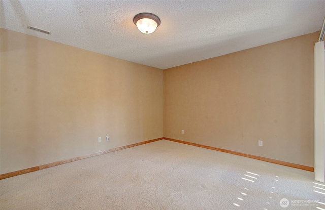 carpeted spare room with baseboards, a textured ceiling, and visible vents